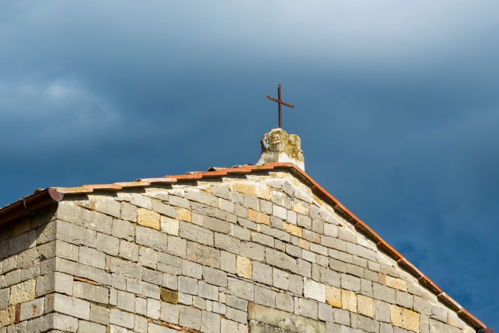 A stone church rooftop with a cross under a dramatic cloudy sky.